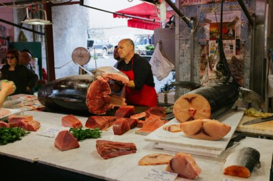 A fish monger at a market slicing a large fish and weighing it