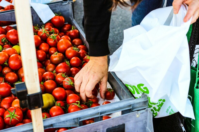 A hand reaches for tomatoes at a market to place into a bag