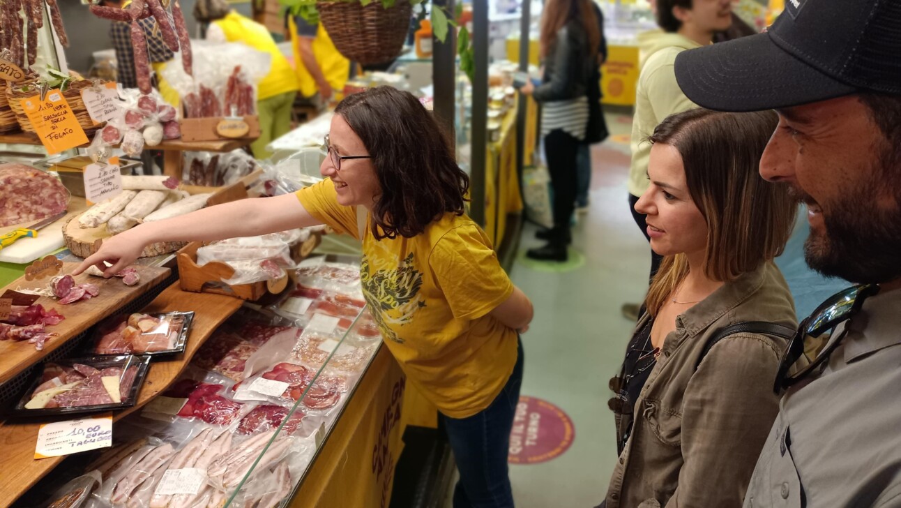 A woman points to the variety of cured meat that she'd like to try at a market stall in Rome, Italy