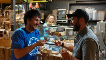 A tour guide and a guest smile as they taste a local Roman speciality at a market